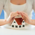 close up of woman protecting house model by hands
